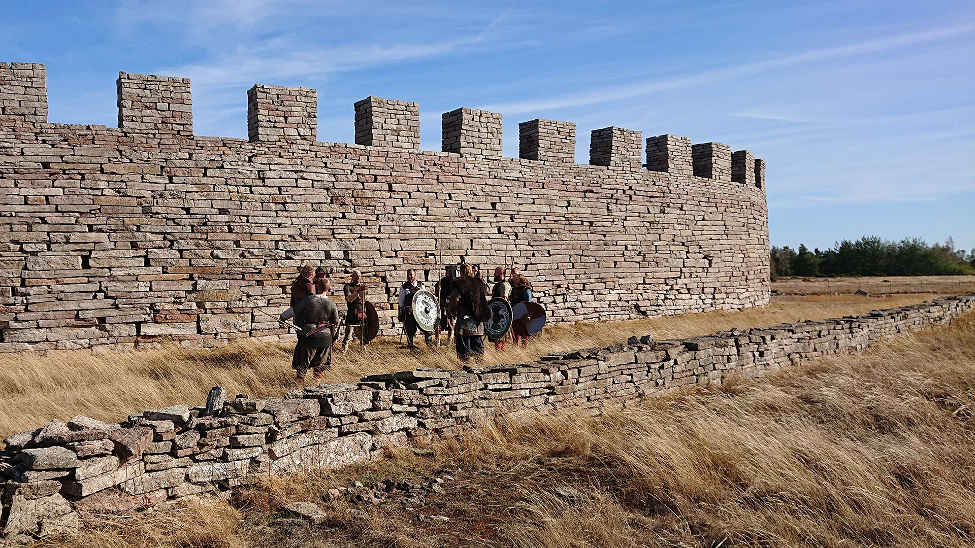 People dressed in warrior clothing are standing outside a big wall.