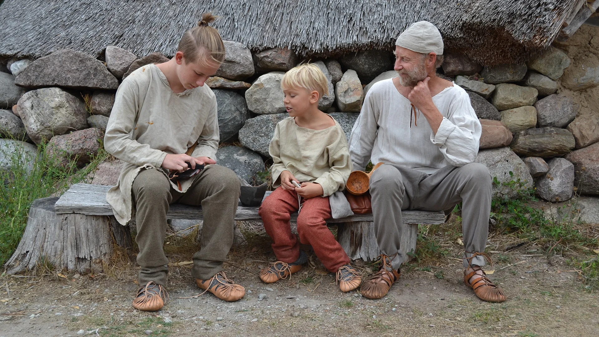 Man and children sitting on a wooden bench wearing simple clothing
