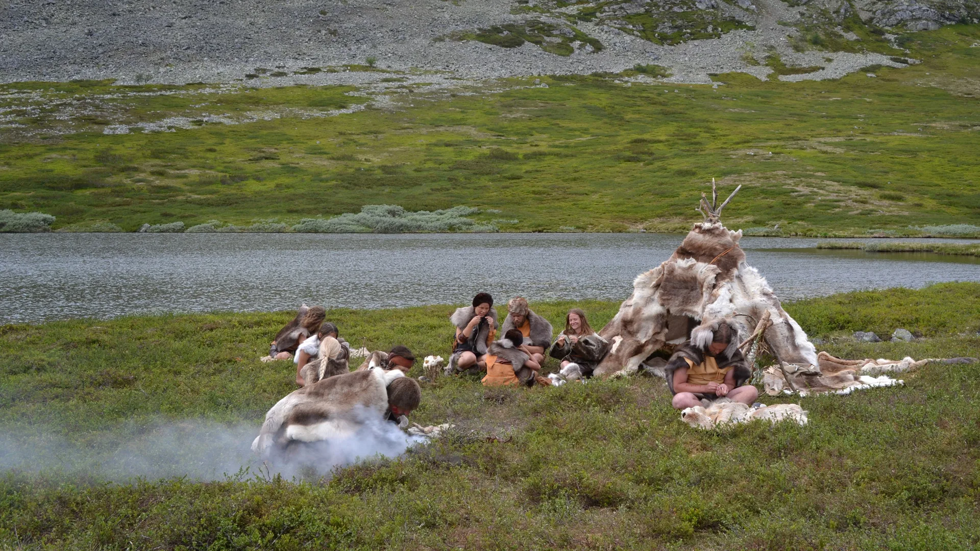 People gathered around a fur-covered shelter in a natural landscape