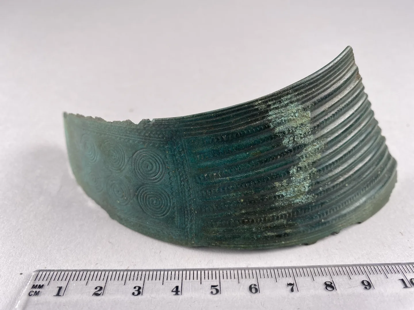 En bit av en bronskrage dekorerad med linjer och cirklar.