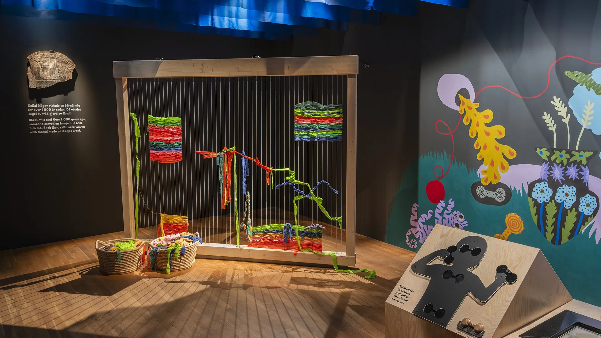 Ett rum med färgglada illiustrationer och en stor vävstol med band i olika färger