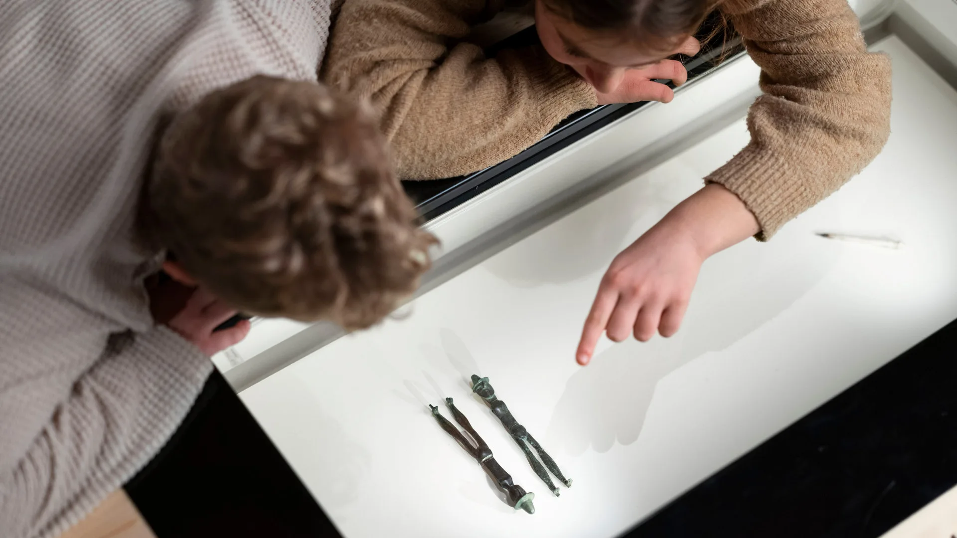 Children pointing to two bronze figurines in a display case