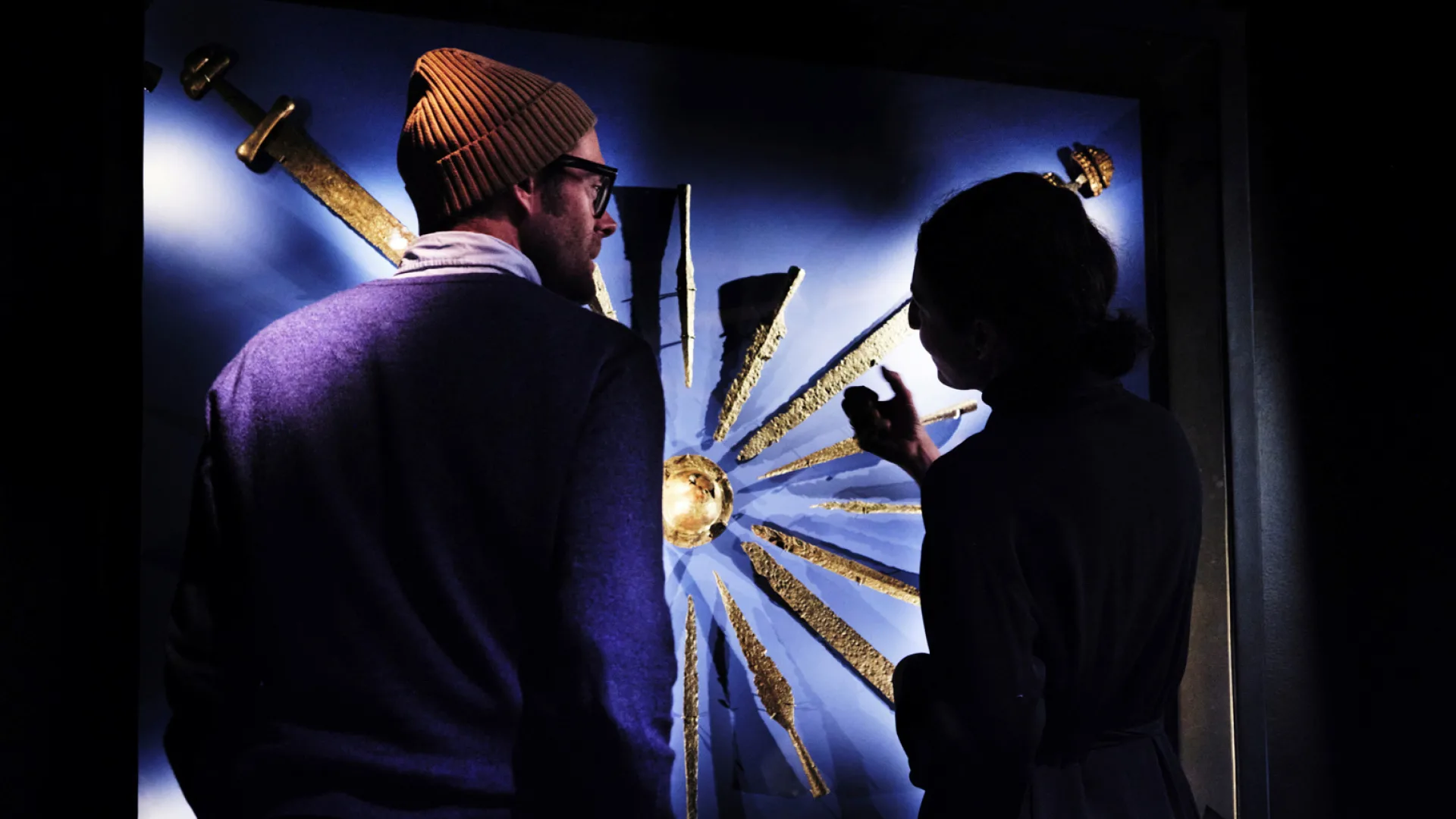 Besökare betraktar svärd i en utställning.