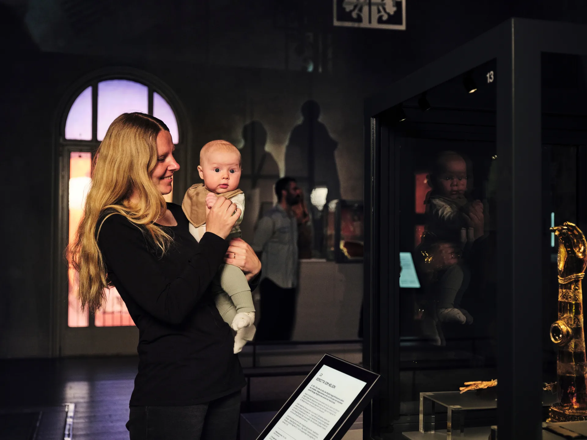 Besökare betraktar en utställning med en baby i famnen.