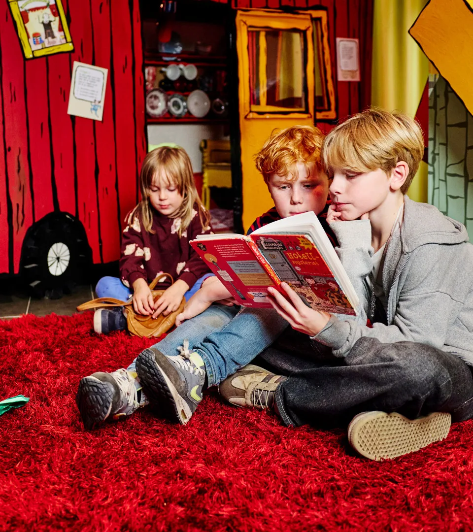 Barn sitter i en utställning och läser bok