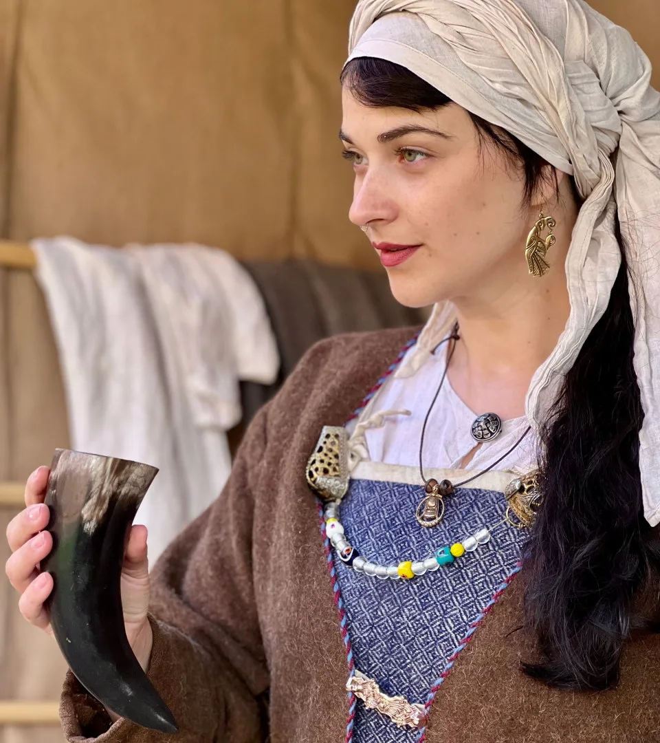 Person med vikingakläder och smycken håller ett dryckeshorn